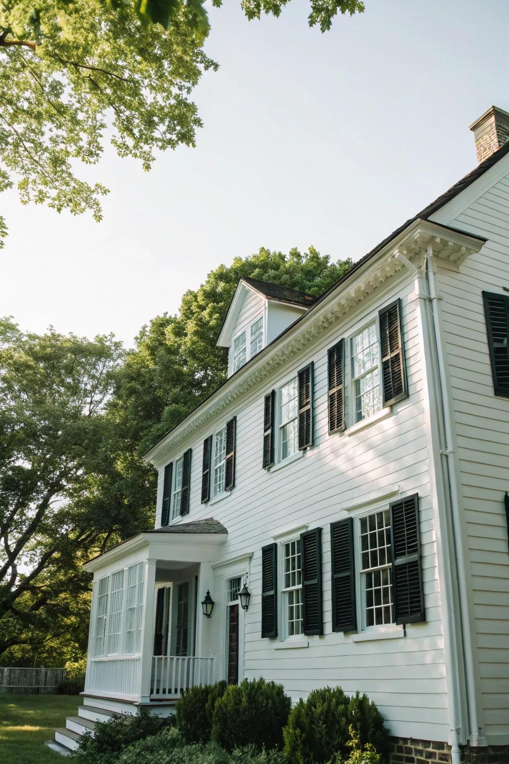 A quintessential colonial dwelling showcasing a pristine white façade beautifully contrasted by ebony shutters.