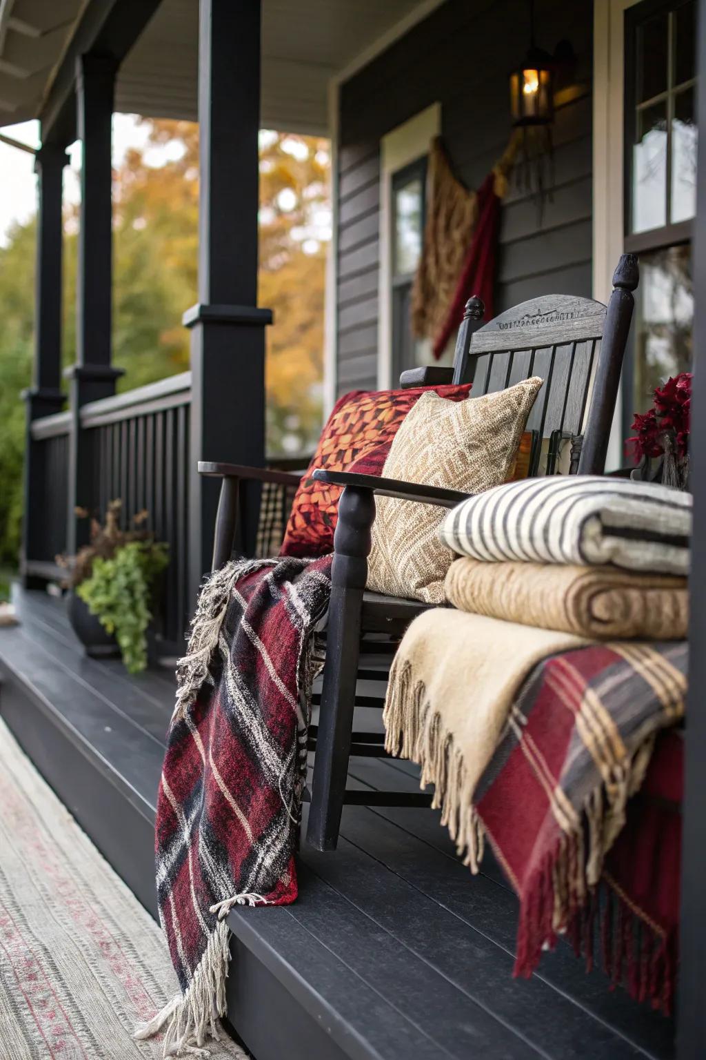 Layered textiles, such as throws and pillows, adding depth to a black porch.